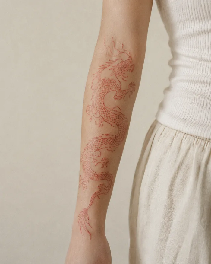 Red fine line dragon tattoo on a forearm
